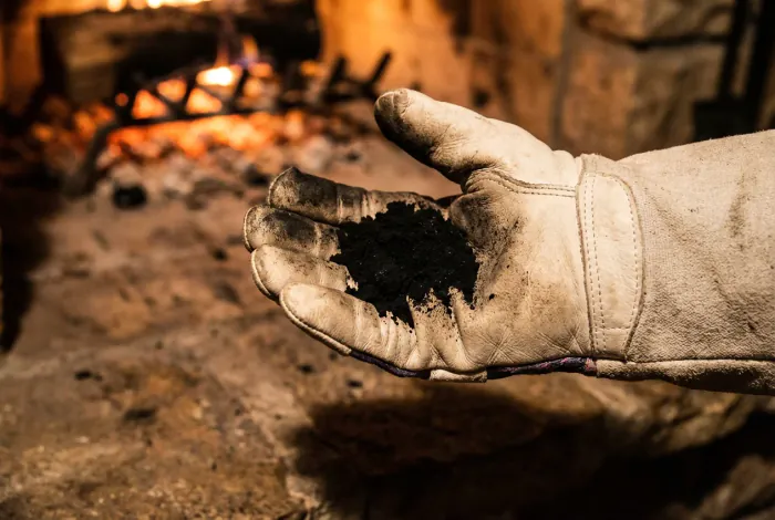 Gros plan d'une main gantée tenant de la suie noire au-dessus d'un foyer de cheminée